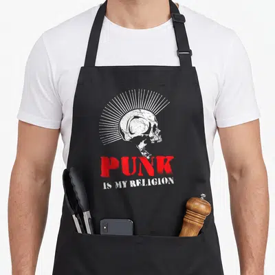 Tablier de cuisine noir avec illustration crâne mohawk blanc et texte Punk Is My Religion en rouge et blanc.