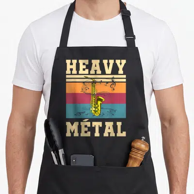 Tablier de cuisine noir avec illustration vintage d'un saxophone doré et le texte Heavy Métal sur fond de bandes colorées.