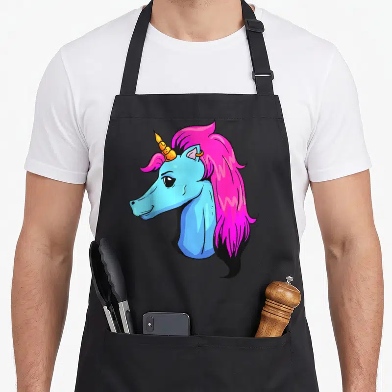 Tablier de cuisine noir avec une illustration de tête de licorne bleue aux cheveux roses et un piercing doré.