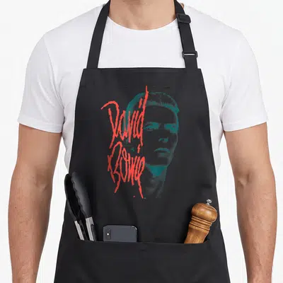 Tablier de cuisine noir avec portrait bleu de David Bowie et signature rouge stylisée sur le devant.