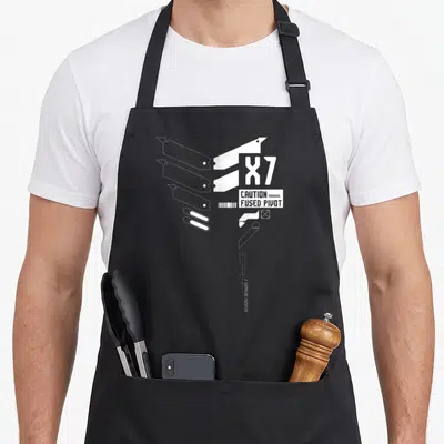 Tablier de cuisine noir avec illustration technique blanche représentant des pièces mécaniques et le texte X7 Caution Fused Pivot.