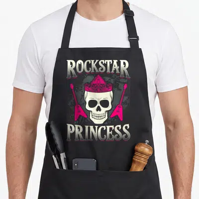 Tablier de cuisine noir avec un crâne portant une couronne rose encadré par deux guitares et le texte Rockstar Princess