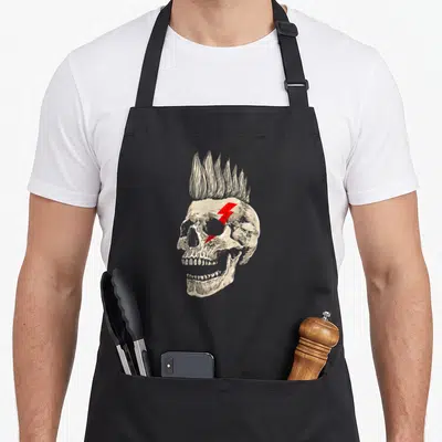 Tablier de cuisine noir avec illustration crâne punk coiffé d'un mohawk et d'un éclair rouge sur l'orbite.