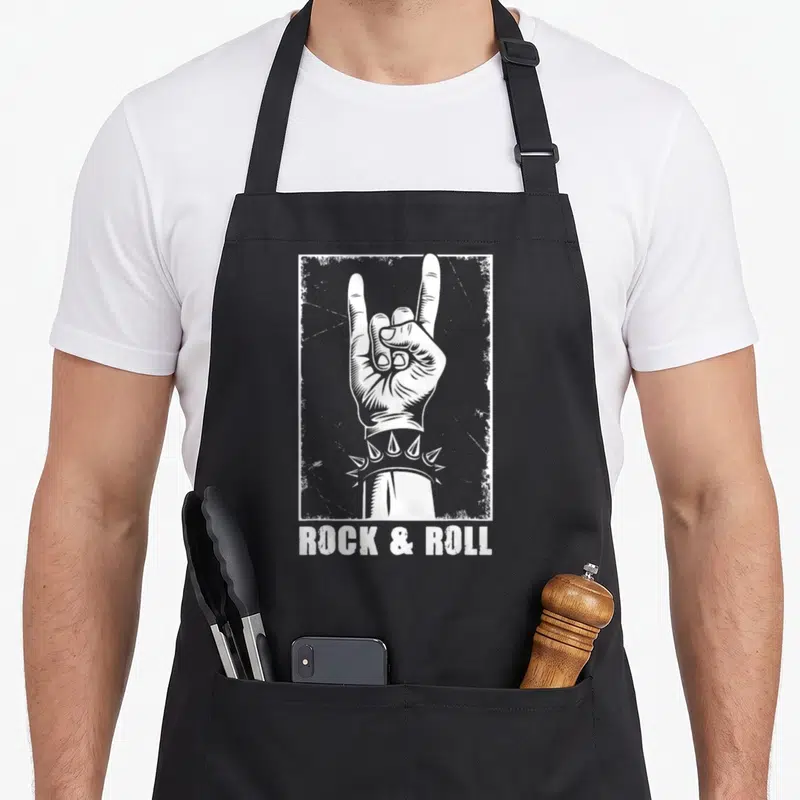 Tablier de cuisine noir avec une illustration blanche montrant un signe de rock et le texte Rock & Roll en bas.