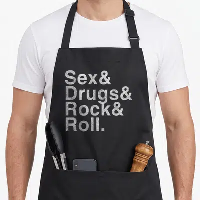 Tablier de cuisine noir avec l'inscription Sex Drugs and Rock and Roll en blanc texturé.