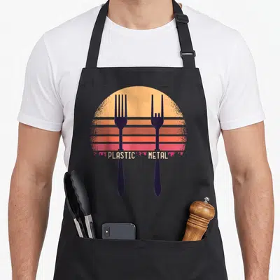 Tablier de cuisine noir avec deux fourchettes noires et le texte Plastic Metal sur un soleil orange et rose.
