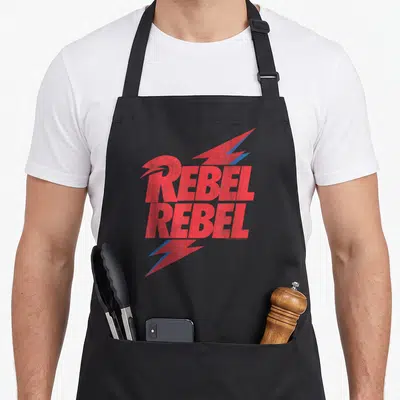Tablier de cuisine noir avec linscription Rebel Rebel en rouge et des éclairs bleus stylisés.