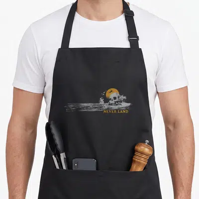 Tablier de cuisine noir avec illustration de Skull Rock, palmiers et texte NEVER LAND orange.