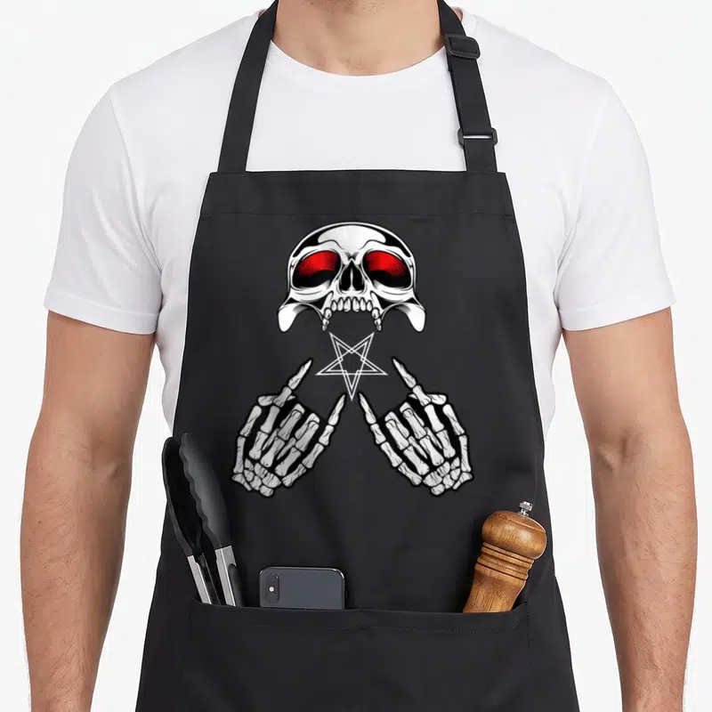 Tablier de cuisine noir avec un crâne aux yeux rouges, des mains squelettiques et une étoile inversée au centre.