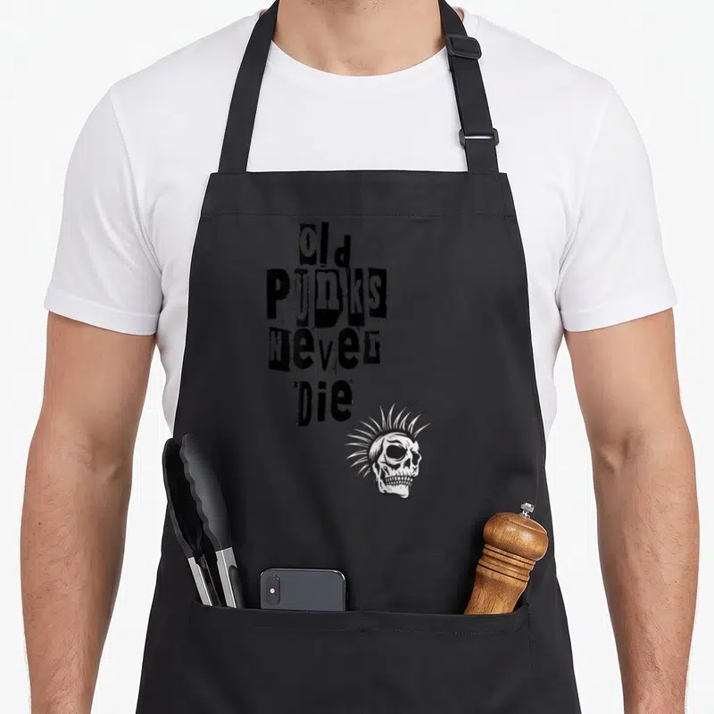 Tablier de cuisine noir avec inscription Les vieux punks ne meurent jamais et illustration de crâne à la mohawk.