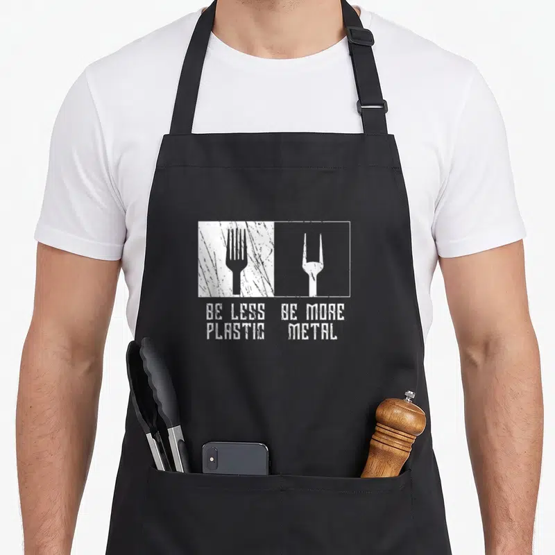 Tablier de cuisine noir avec illustration blanche d'une fourchette et du texte Be Less Plastic Be More Metal.