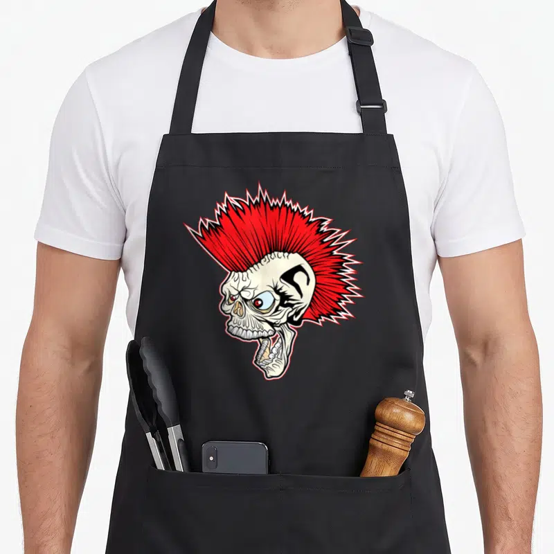 Tablier de cuisine noir avec un crâne au mohawk rouge vif et une expression punk rock agressive.