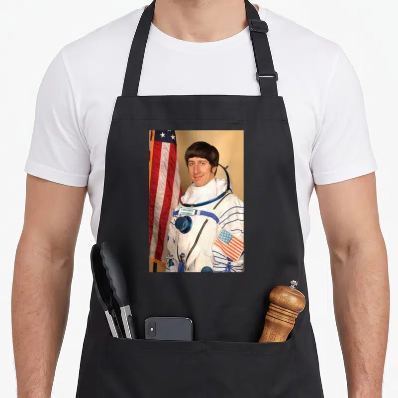 Tablier de cuisine noir avec Howard Wolowitz en combinaison spatiale blanche et drapeau américain.