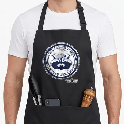 Tablier de cuisine noir avec un badge circulaire illustrant le visage d'un raccoon et l'inscription Rocket Powered en bleu.