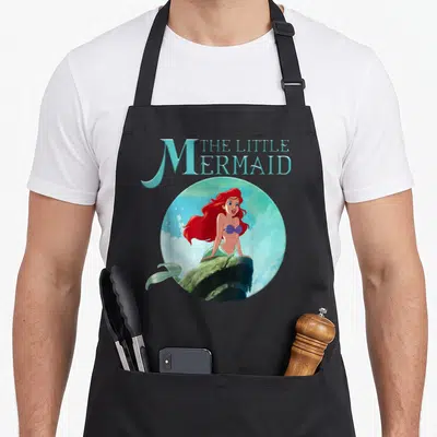 Tablier de cuisine noir avec Ariel du Little Mermaid posée sur une pierre circulaire