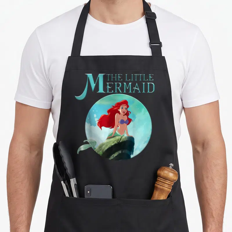 Tablier de cuisine noir avec Ariel du Little Mermaid posée sur une pierre circulaire
