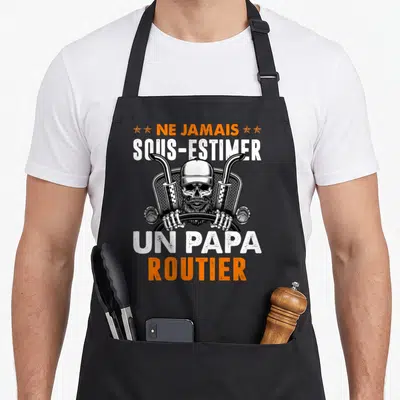 Tablier de cuisine noir avec un crâne barbu coiffé d'une casquette entre deux tuyaux d'échappement et le texte Ne jamais sous-estimer un papa routier.
