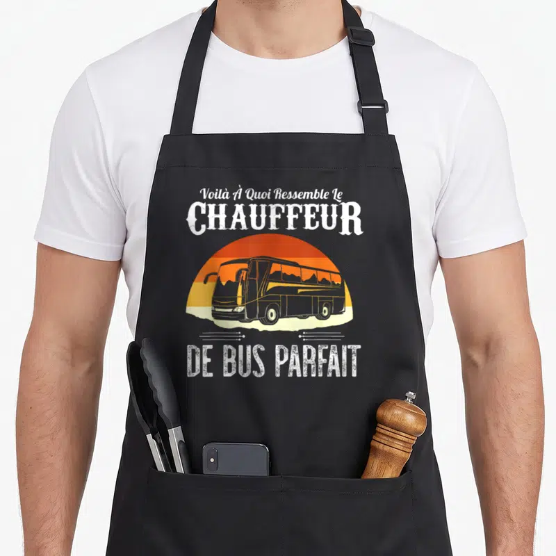 Tablier de cuisine noir avec illustration de bus rétro et texte blanc sur fond de soleil orange dégradé.