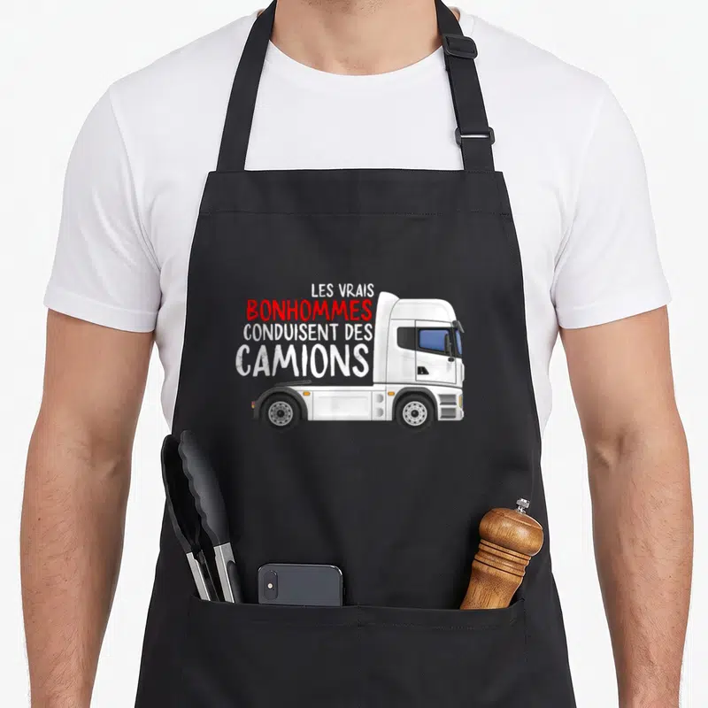 Tablier de cuisine noir avec illustration de tracteur blanc et texte Les vrais bonhommes conduisent des camions en rouge et blanc.