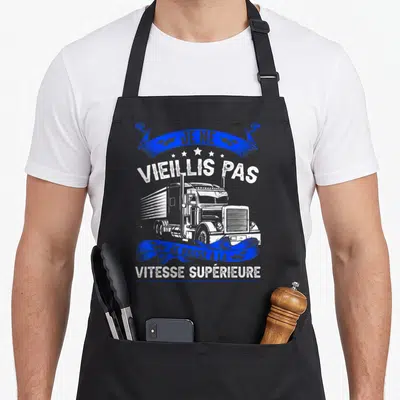 Tablier de cuisine noir avec illustration de camionneur et inscription Je ne vieillis pas je passe à la vitesse supérieure en bleu et blanc.