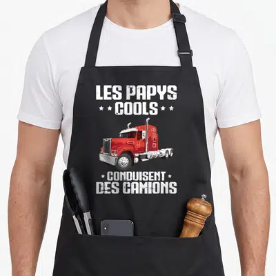 Tablier de cuisine noir avec illustration d'un camion rouge et le texte Les Papys Cools Conduisent Des Camions en typographie blanche usée.