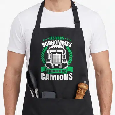 Tablier de cuisine noir avec illustration frontale d'un camion blanc et texte vert et blanc Les vrais bonhommes conduisent des camions.