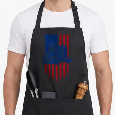 Tablier de cuisine noir avec illustration semi-truck bleu sur fond drapeau américain rouge et blanc déstructuré.