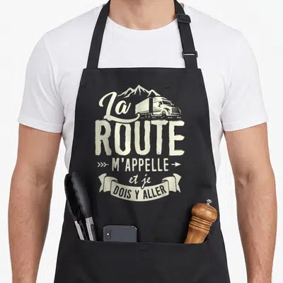 Tablier de cuisine noir avec illustration vintage d'un camion routier et le texte La Route m'appelle et je dois y aller en typographie blanche.