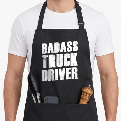 Tablier de cuisine noir avec l'inscription en blanc Badass Truck Driver au style usé et texturé.