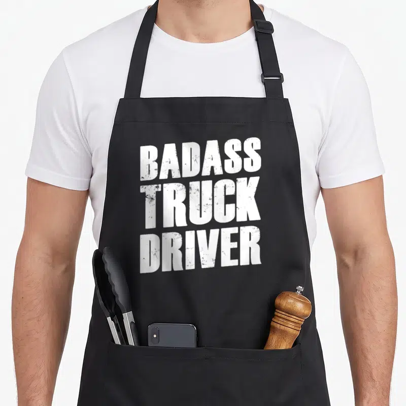 Tablier de cuisine noir avec l'inscription en blanc Badass Truck Driver au style usé et texturé.