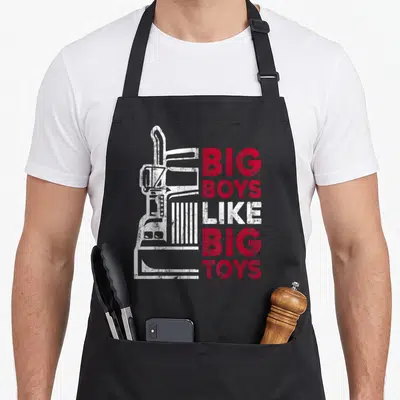 Tablier de cuisine noir avec illustration de camion blanc et texte Big Boys Like Big Toys en rouge et blanc.