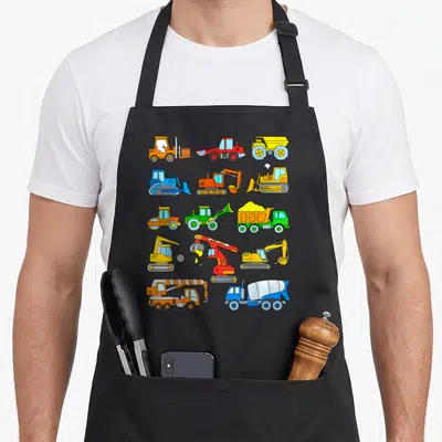 Tablier de cuisine noir avec pelles, camions et bulldozers colorés en style dessin animé.