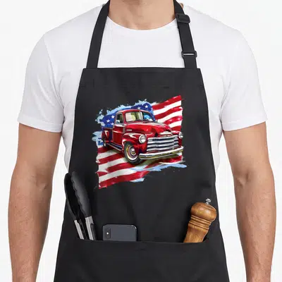 Tablier de cuisine noir avec illustration d'un camion pick-up rouge vintage devant un drapeau américain stylisé.