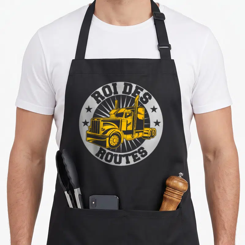 Tablier de cuisine noir avec illustration circulaire d'un camion jaune et texte Roi des Routes entouré d'étoiles grises.