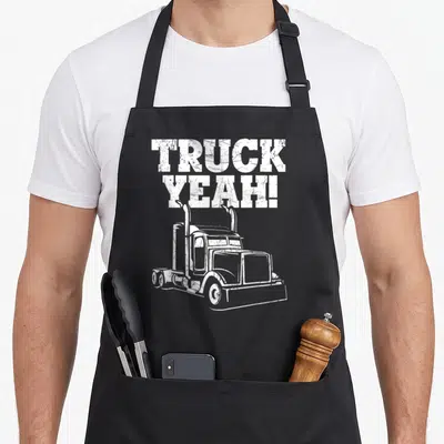 Tablier de cuisine noir avec illustration de camion américain et texte TRUCK YEAH. en lettres blanches usées.