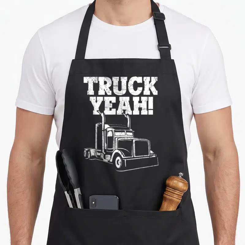 Tablier de cuisine noir avec illustration de camion américain et texte TRUCK YEAH. en lettres blanches usées.