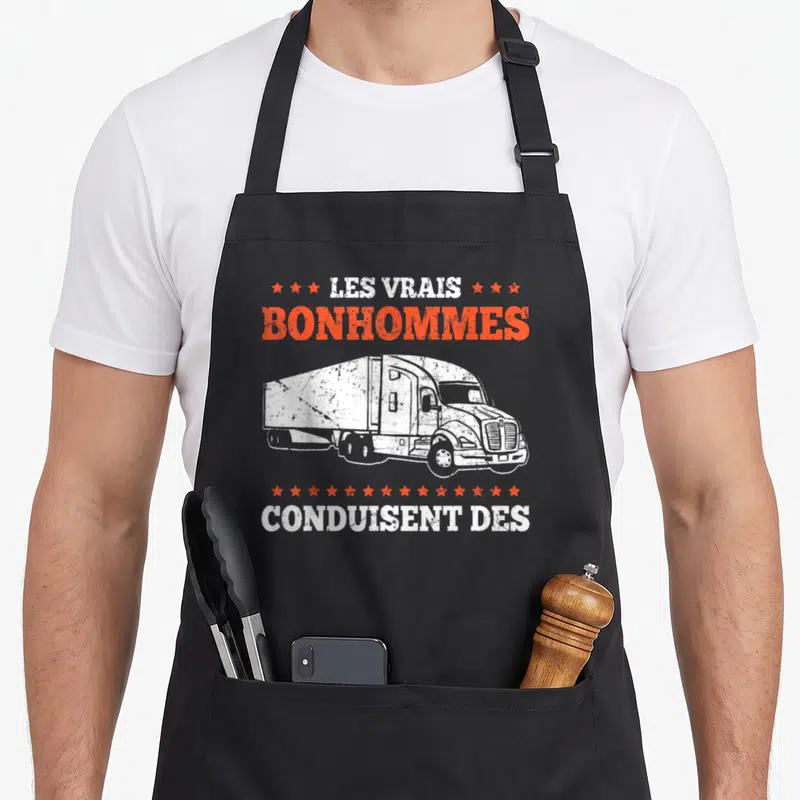 Tablier de cuisine noir avec illustration semi-remorque blanche et texte Les Vrais Bonhommes Conduisent Des Camions en orange et blanc.