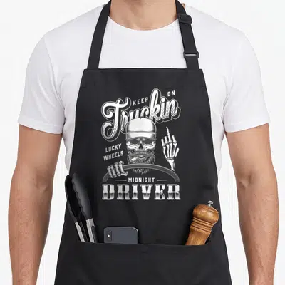 Tablier de cuisine noir avec un crâne barbu tenant un volant et le texte Keep On Truckin Lucky Wheels Midnight Driver.