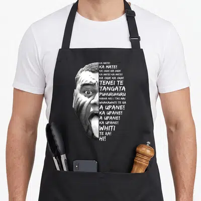 Tablier de cuisine noir avec portrait monochrome d'un joueur effectuant le Haka et des textes en maori alignés à droite.