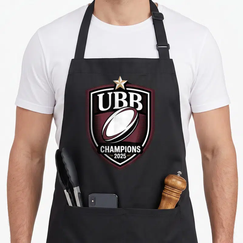 Tablier de cuisine noir avec un blason UBB Champions 2025, une étoile dorée et un ballon de rugby stylisé en bordeaux et blanc.