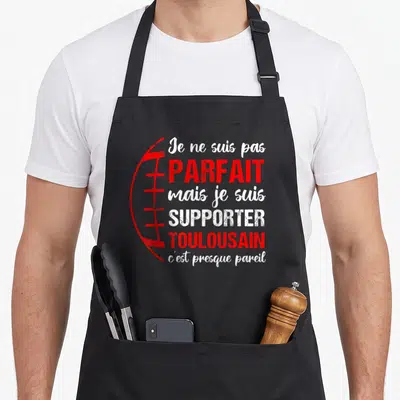 Tablier de cuisine noir avec texte blanc et rouge et dessin de ballon de rugby sur le côté gauche.