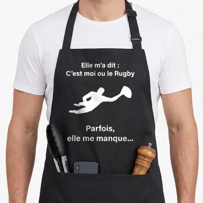 Tablier de cuisine noir avec silhouette blanche d'un joueur de rugby et texte humoristique sur fond uni.
