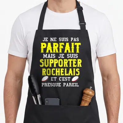 Tablier de cuisine noir avec texte jaune et blanc Je ne suis pas parfait supporter rochelais et deux ballons de rugby blancs.
