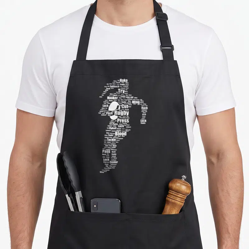 Tablier de cuisine noir avec une silhouette féminine constituée de mots blancs liés au rugby tels que Try, Pass, Tackle et Blood.