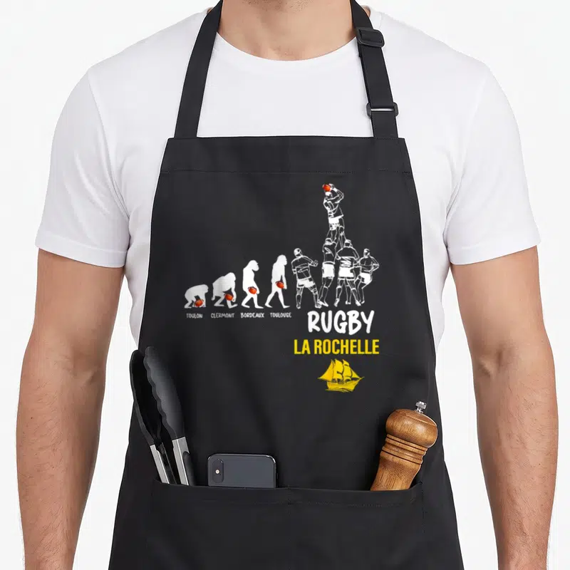 Tablier de cuisine noir avec illustration évolution rugby citant Toulon Clermont Bordeaux Toulouse et La Rochelle en bas.
