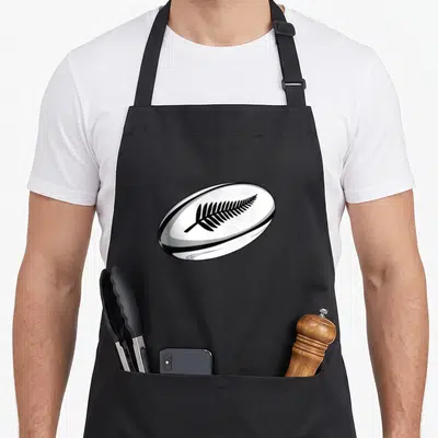 Tablier de cuisine noir avec illustration d'un ballon de rugby blanc portant une fougère noire stylisée au centre.