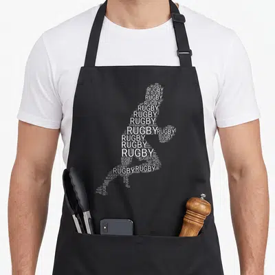 Tablier de cuisine noir avec une silhouette de joueur de rugby composée du mot Rugby répété en blanc.