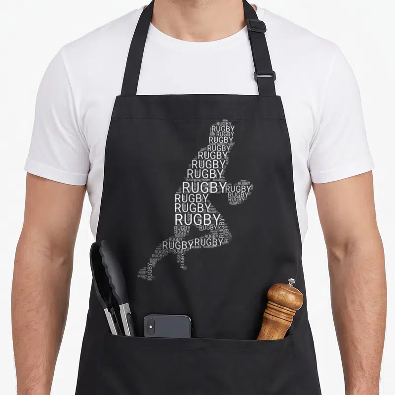 Tablier de cuisine noir avec une silhouette de joueur de rugby composée du mot Rugby répété en blanc.