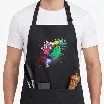 Tablier de cuisine noir avec illustration artistique d'un ballon de rugby aux éclats de peinture colorés.