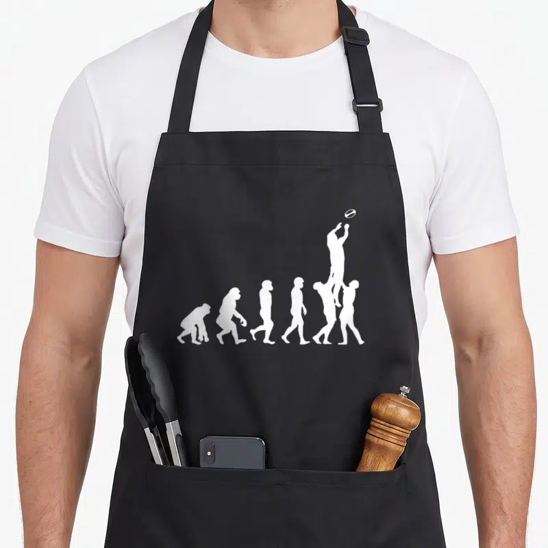 Tablier de cuisine noir avec silhouette blanche représentant l'évolution humaine vers le rugby et un ballon ovale.